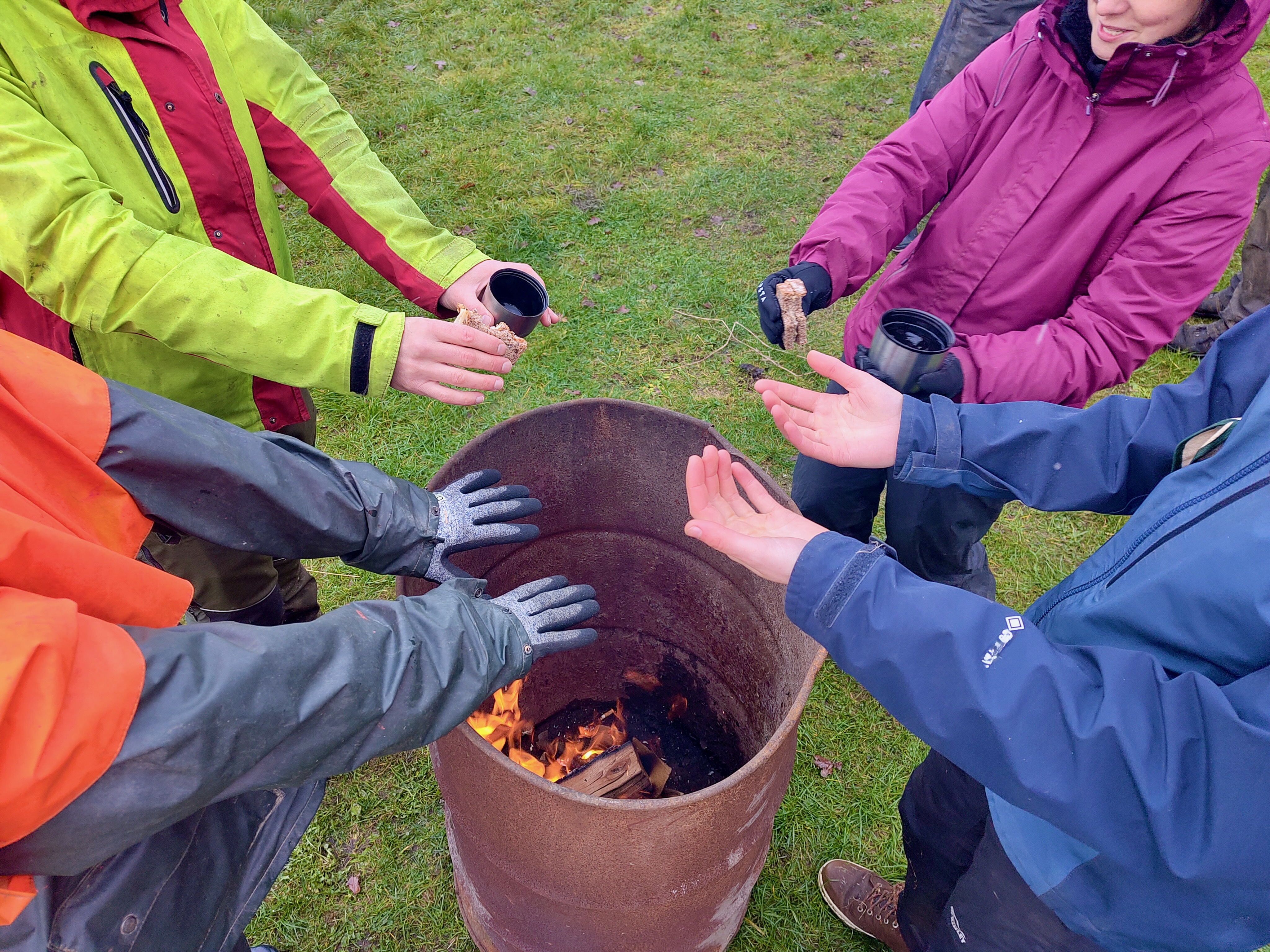 Acht Handpaare wärmen sich am Feuer über einer Tonnen