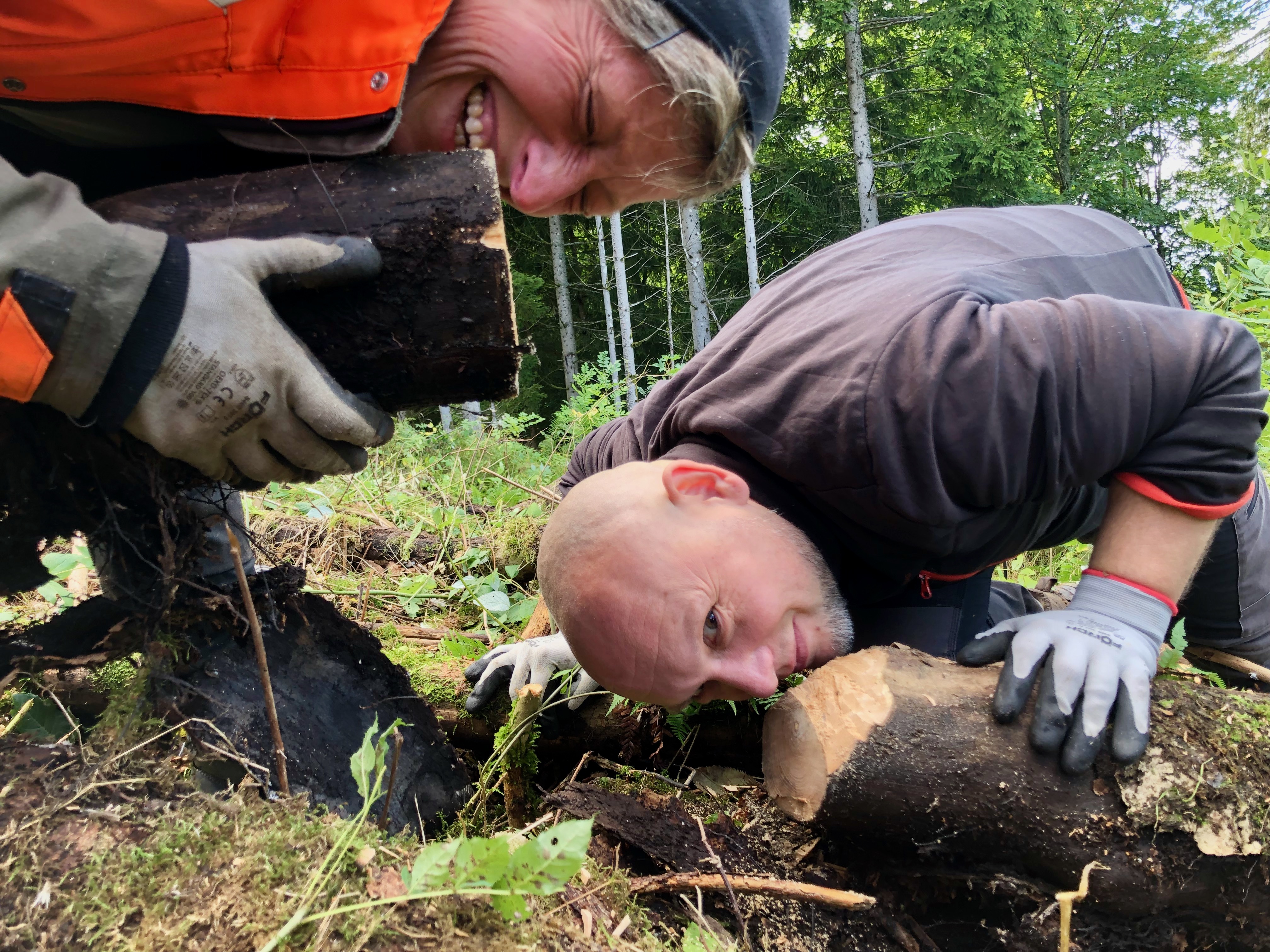 Zwei Menschen knien am Boden und riechen an Holzstämmen
