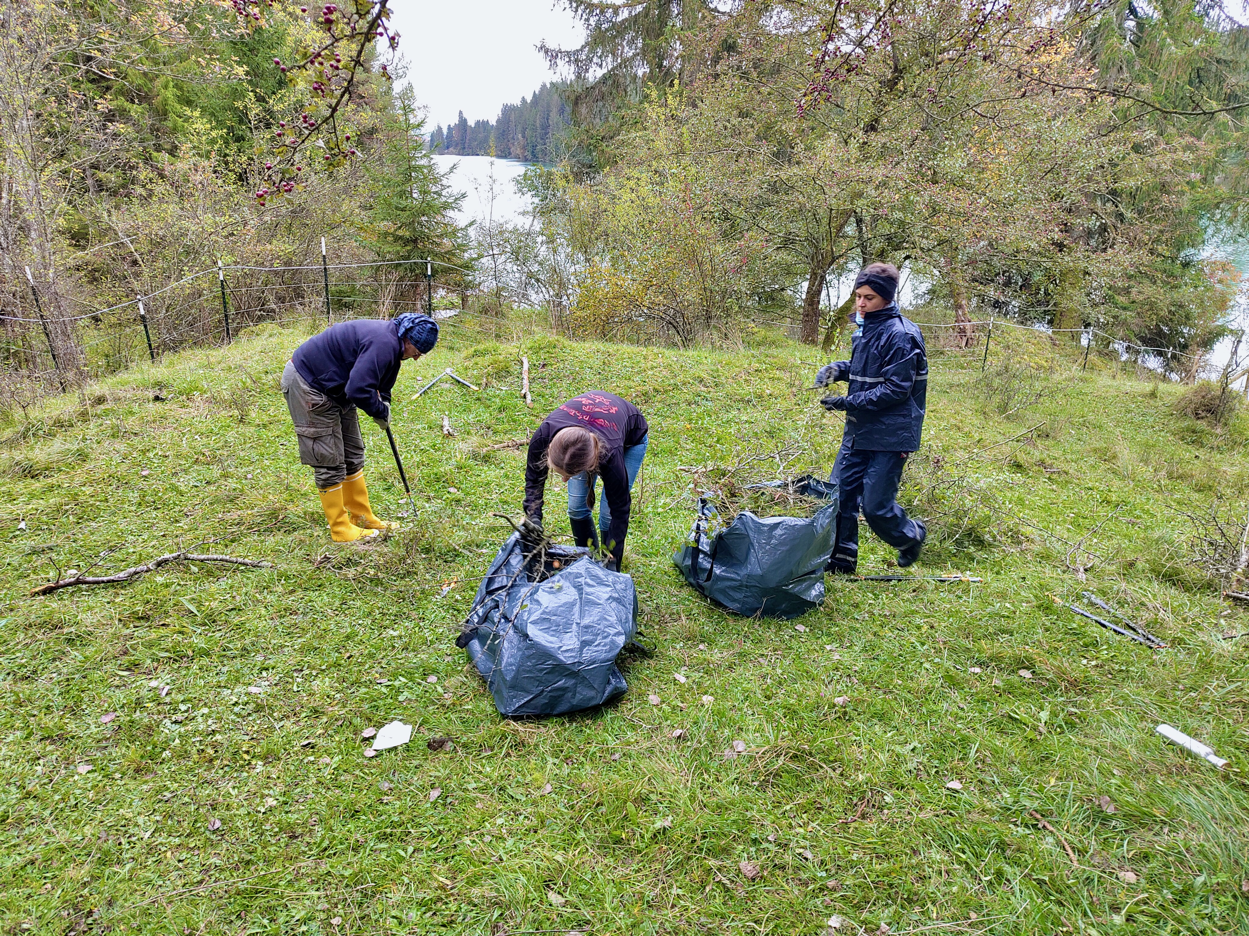 Drei Menschen auf einem kleinen grünen Grashügel, im Hintergrund ein Fluss