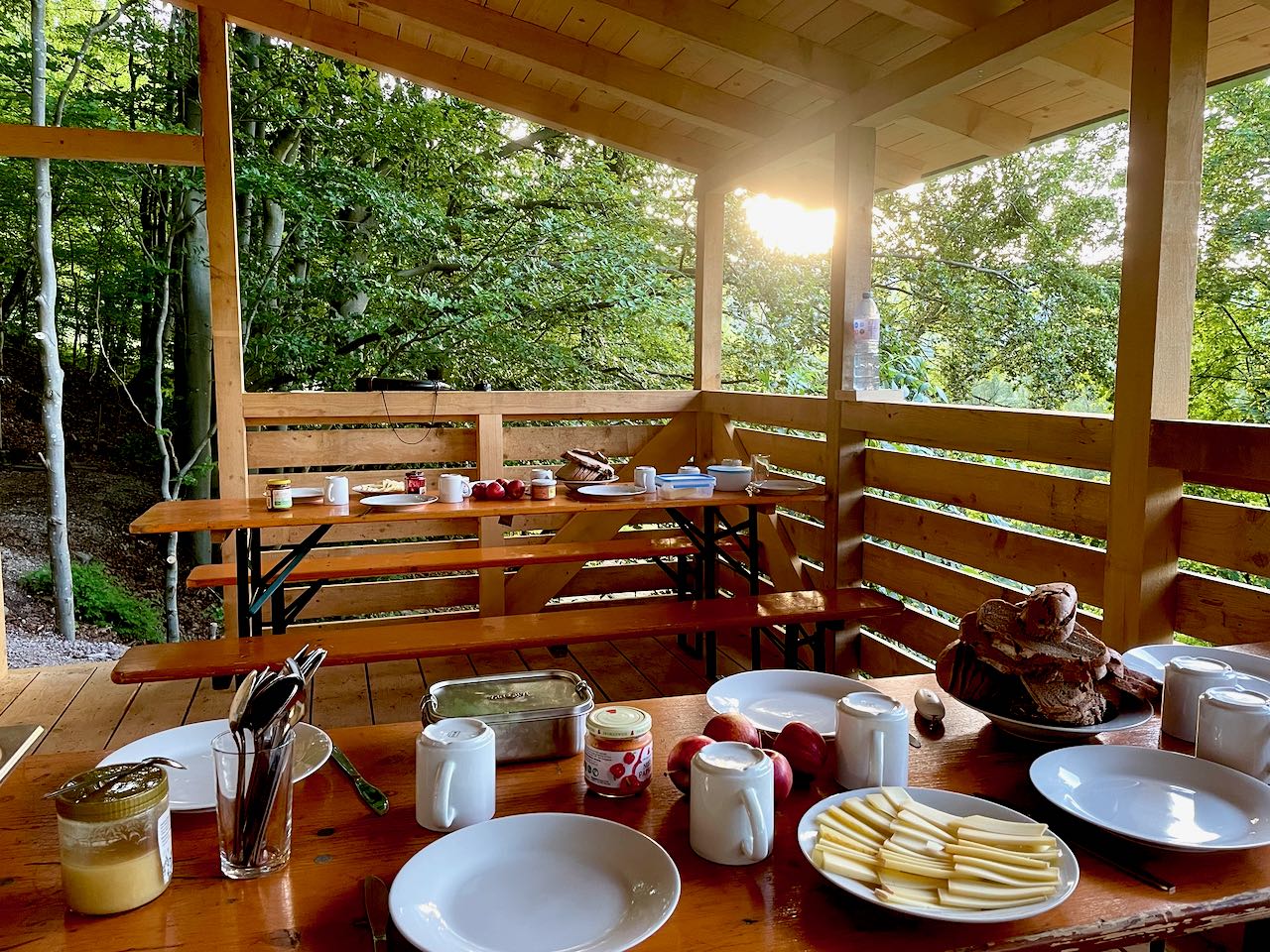 Frühstück ist fertig Die tiefstehende Sonne scheint auf eine Holzveranda auf der ein Frühstück aufgebaut ist