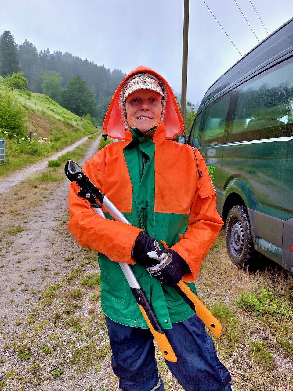 Eine Frau in einer Regenjacke hat eine Astschere in den Händen