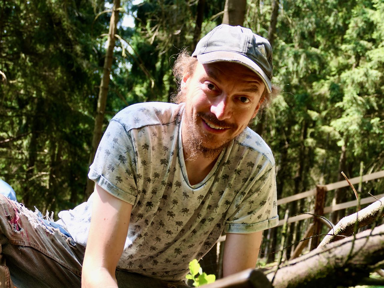 Ein Mann mit Mütze schaut im Wald den Betrachter an