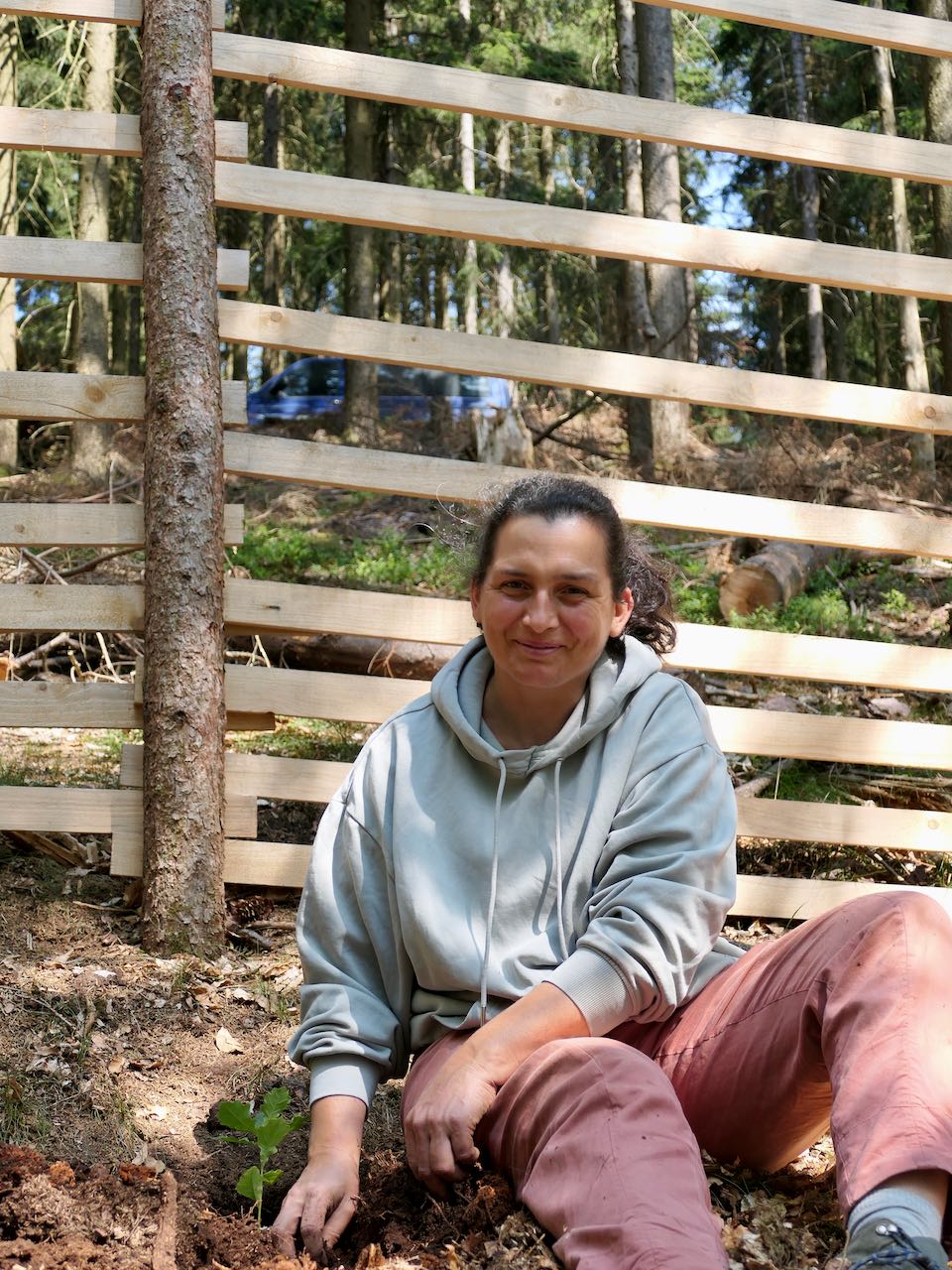 Katja beim Eichen pflanzen in Unterschönau Eine Frau sitzt vor einem Holzzaun im Wald.