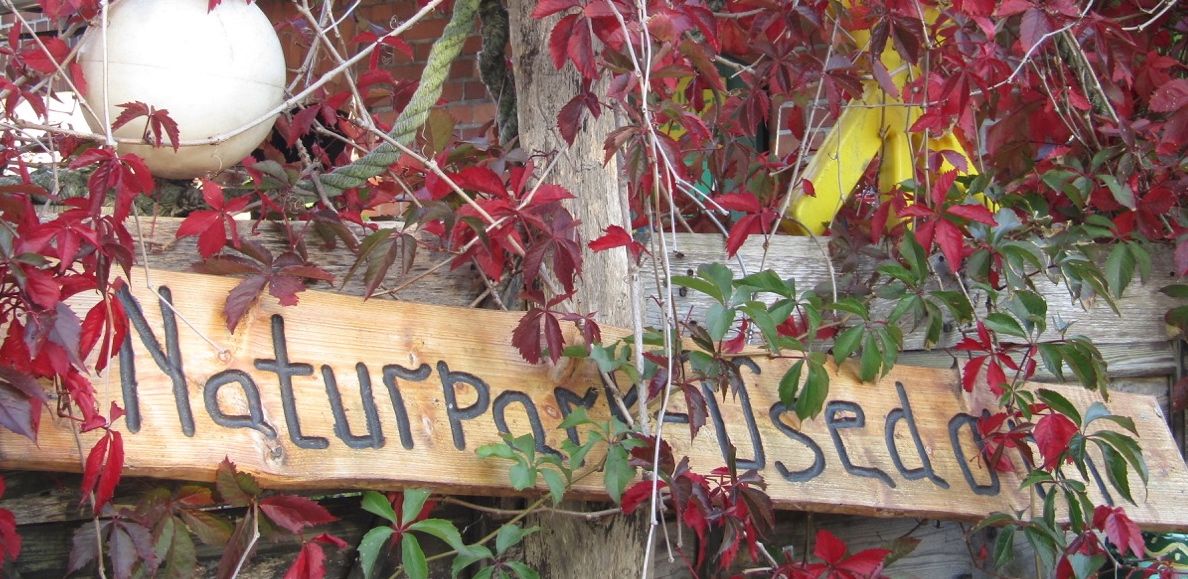 Ein Holzschild sagt wie der Naturpark heisst. 