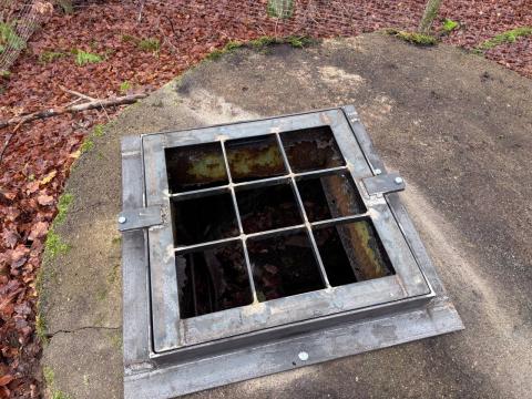 Eine vergitterte Öffnung eines Betonblocks im Wald