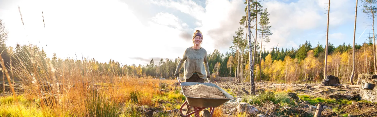 Frau schiebt Schubkarre mit Material zur Grabenverfüllung im Moor
