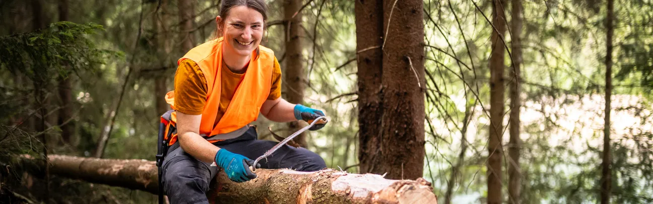 Lächelnde Frau sitzt auf Baumstamm mit Schälmesser