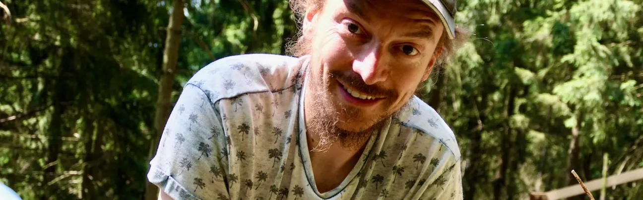Ein Mann mit Mütze schaut im Wald den Betrachter an