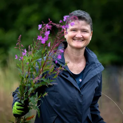 Lächelnde Frau hält Pflanze mit rosa Blüten