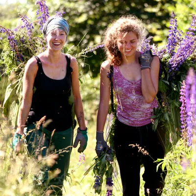 Zwei lächelnde Teilnehmerinnen mit einer großen Taschen voller Lupinen auf dem Rücken