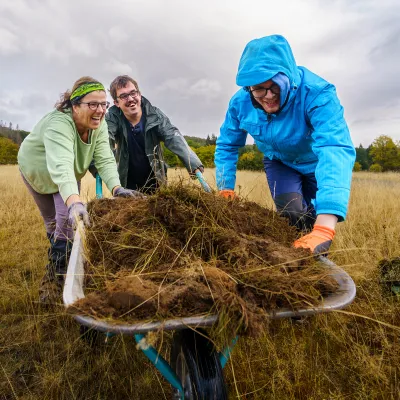 Menschen mit udn ohen Behinderung schieben geladenen Schubkarren