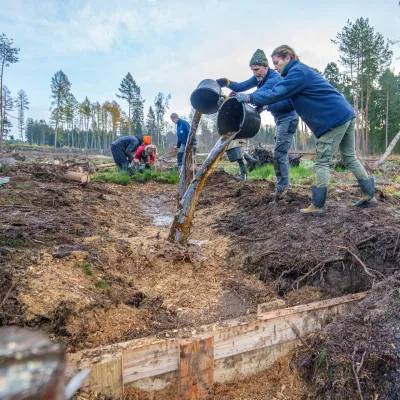 Teilnehmende kippen Wasser aus Eimern in den Graben