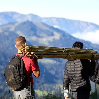 Teilnehmer tragen Bambusstäbe durch eine Berglandschaft
