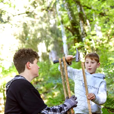 Zwei Teilnehmer die Bambusstäbe mit einem Hammer in die Walderde schlagen.