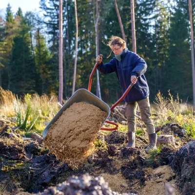 Frau die die Ladung ihrer Schubkarre auskippt