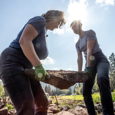 2 Frauen tragen schweren Stein