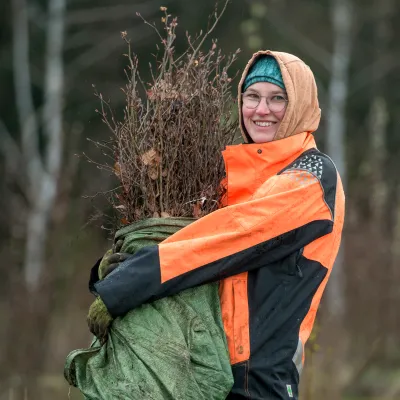 Lächelnde Frau trägt einen großen Beutel mit Setzlingen