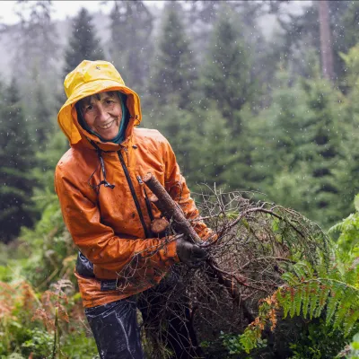 Lächelnde Teilnehmerin mit Regenjacke beim Abtransport von Zweigen