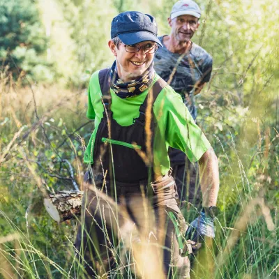 Zwei lächelnde Teilnehmende tragen einen entnommenen Baum