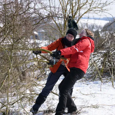 Zwei Frauen in roten Jacken ziehen gemeinsam an Ast