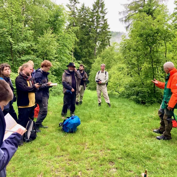 Ein Mann steht im Wald vor einer Gruppe Menschen