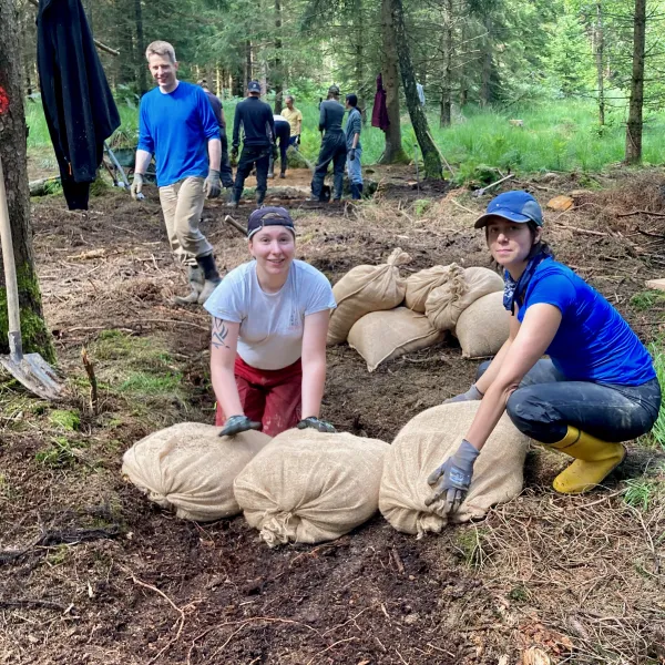 Zwei Knien im Wald vor drei prall gefüllten Jutesäcken