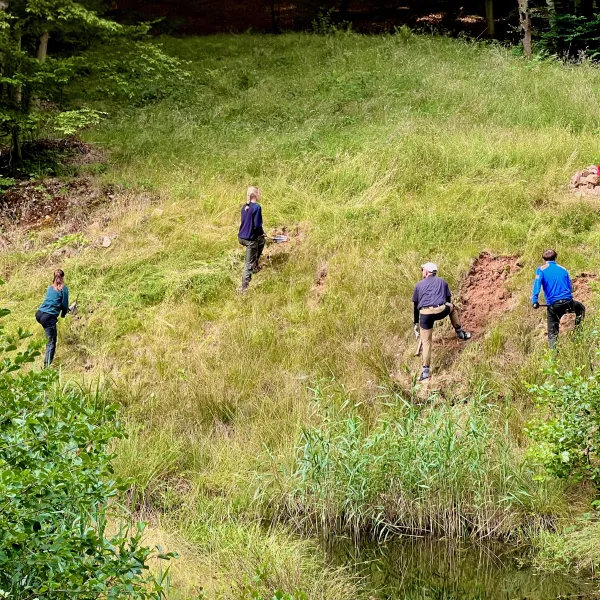 Vier Menschen stehen hinter einem Weiher verteilt am Hang