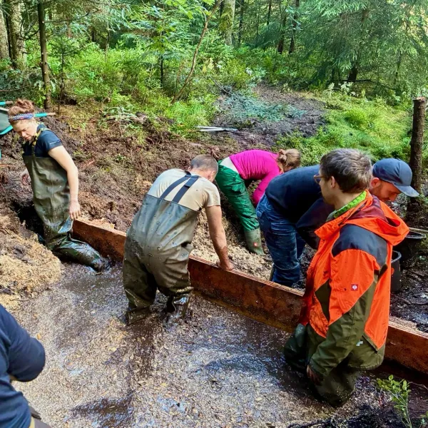 Menschen stehen an einer Bohlenwand im Wasser eines Grabens.