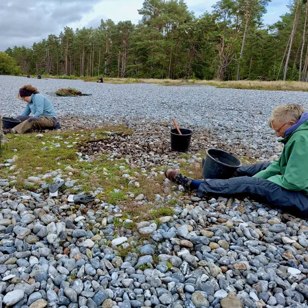 Zwei Frauen sitzen auf einer Kiesfläche, am Rande Hochwald