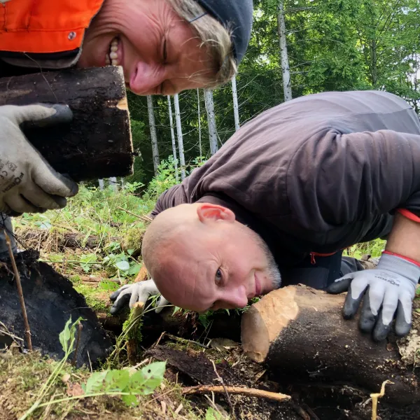 Zwei Menschen knien am Boden und riechen an Holzstämmen