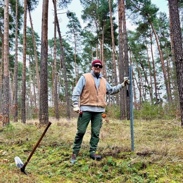 Ein Mann mit Schutzbrille steht im Wald an einem Zaun