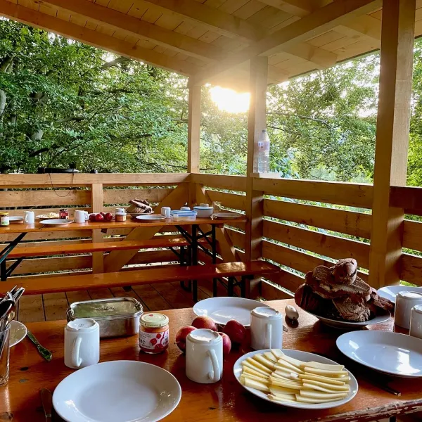 Die tiefstehende Sonne scheint auf eine Holzveranda auf der ein Frühstück aufgebaut ist