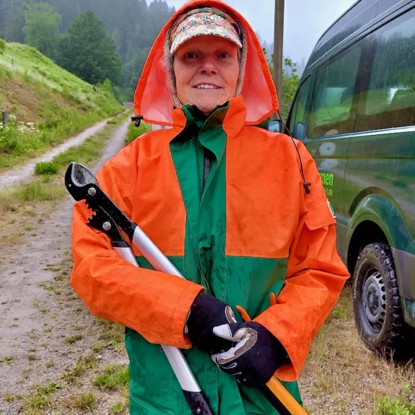 Eine Frau in einer Regenjacke hat eine Astschere in den Händen