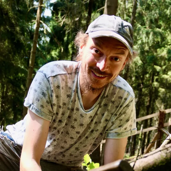 Ein Mann mit Mütze schaut im Wald den Betrachter an