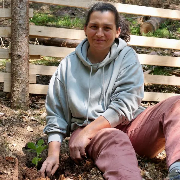 Eine Frau sitzt vor einem Holzzaun im Wald.