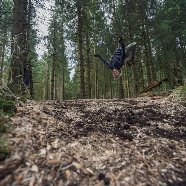 Person macht einen Salto über einem mit Sägemehl und Hackschnitzeln verfüllten ehemaligen Entwässerungsgraben