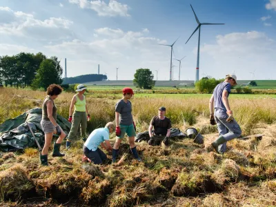 Freiwillige auf Wiese mit Windrädern im Hintergrund